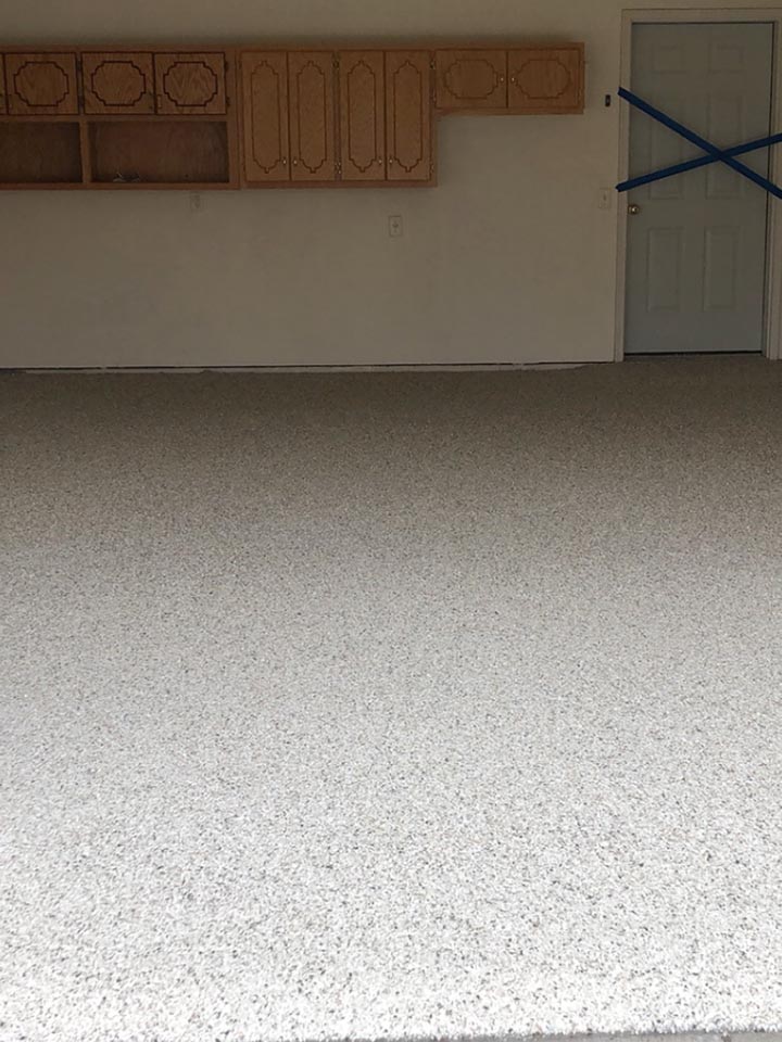 Residential garage with tan and beige flake floor, oak cabinets